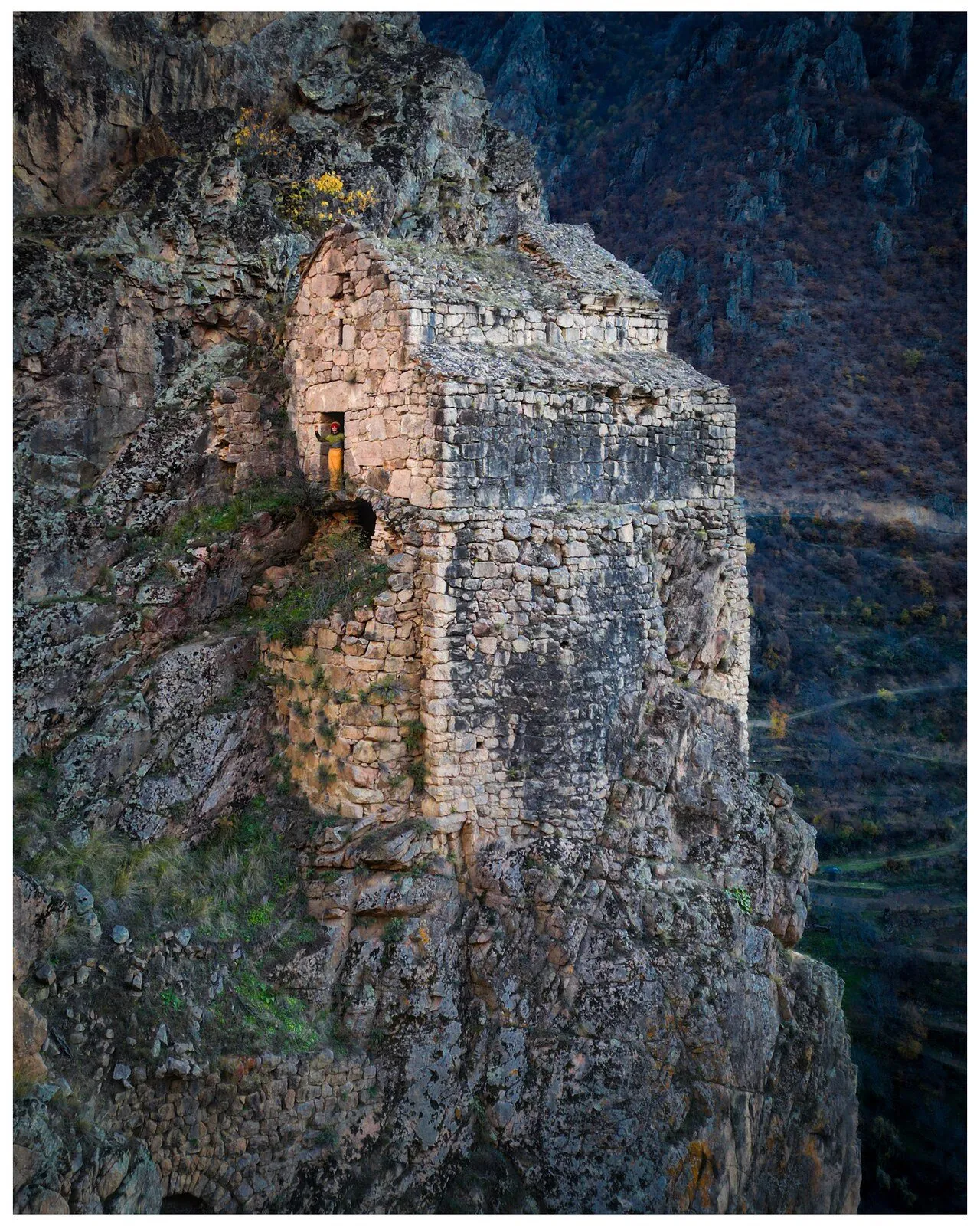 A stone church ruin clinging to a sheer cliff in Artvin, a lone figure lit in the doorway